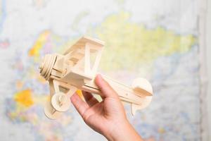 Close-up of wooden toy plane in children's hands on world map background in kids room at home. Childhood dream imagination and Travel concepts.