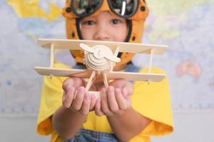 Little girl in a pilot hat holding a toy plane in her hands having fun in kids room at home. Happy child girl at home dreaming of travel and tourism. Childhood dream imagination and Travel concepts. photo