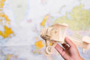 Close-up of wooden toy plane in children's hands on world map background in kids room at home. Childhood dream imagination and Travel concepts. photo