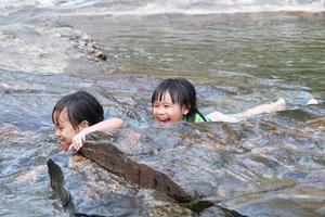 Cute Asian children wearing life jackets are enjoying playing in the river. Two little sisters enjoyed swimming in the stream. Healthy Summer Activities for Kids. photo