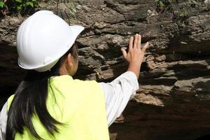 la investigadora geóloga asiática toca rocas con las manos para analizar superficies en un parque natural. geólogo de exploración en el campo. concepto de piedra y ecología. foto