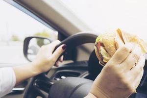 Lady driving car while eating hamburger photo
