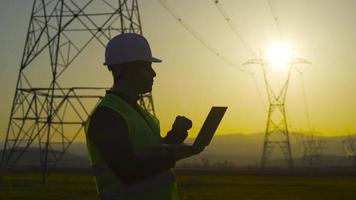 torri elettriche e ingegnere di lavoro. ingegnere che lavora davanti a torri elettriche, sagoma di ingegnere al tramonto. ingegnere elettrico. video