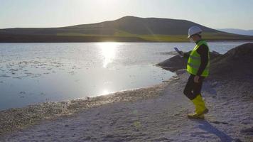 medio ambiente y contaminación del agua. trabajando en la contaminación del lago, el ingeniero examina los desechos químicos acumulados por el lago y continúa trabajando en la tableta. video