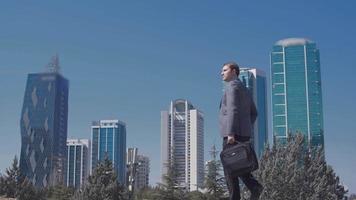 edificios comerciales en la ciudad y hombre de negocios con bolsa. hombre de negocios caminando frente a edificios comerciales en la ciudad. hombre de negocios moderno en traje. video