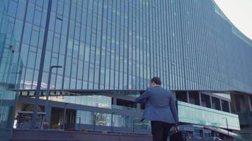 homme d'affaires marchant au bâtiment de l'entreprise. homme d'affaires moderne avec sac se rend au centre d'affaires en regardant sa montre. homme d'affaires en costume avec sac. video