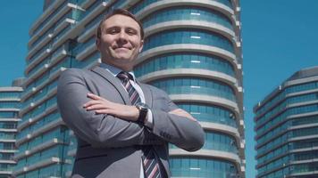 Luxury buildings and businessman. Businessman looking at camera in front of luxury buildings folds his arms and smiles.  Modern businessman in suit. video