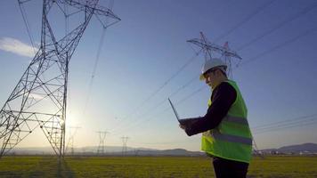 eltorn och arbetande ingenjör. ingenjör undersöker och arbetar på dator framför elektriska torn. video