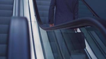 hombre de negocios con bolsa subiendo la escalera mecánica. hombre de negocios con maletín frente a un edificio de negocios de lujo sube la escalera mecánica. imagen de edificio moderno y hombre de negocios moderno. video