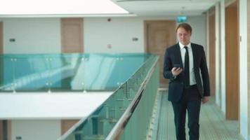 Businessman talking on the phone in the hallway. A man walking down the aisle at work is talking on the phone. Corporate and modern looking businessman. video