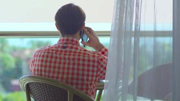 llamada telefónica en el balcón del hotel. hombre de negocios sentado en el balcón del hotel y hablando por teléfono. video