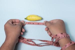 la mano de un hombre está midiendo un plátano pequeño usando una cinta métrica, concepto de tamaño de genitales masculinos pequeños foto