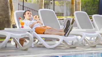 Cocktail by the pool at the hotel. Man lying on a sun lounger by the pool is drinking a cocktail. He is dancing and happy. video