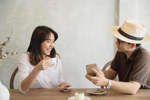 hombre y mujer casuales hablando alegremente mientras toman café y miran el teléfono móvil - estilo de vida feliz en la cafetería foto