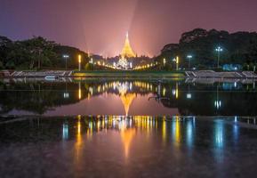 The double reflection of Shwedagon pagoda on the water at night. photo