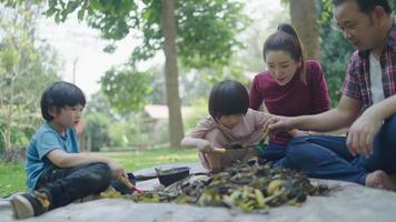 een gezin van twee zonen helpt bij het uitvoeren van stukjes fruit en groenten om te leren hoe ze natuurlijke compost kunnen maken. in de voortuin op vakantie video