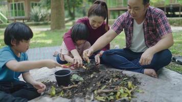 een gezin van twee zonen helpt bij het uitvoeren van stukjes fruit en groenten om te leren hoe ze natuurlijke compost kunnen maken. in de voortuin op vakantie video