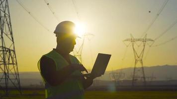 ingeniero eléctrico trabajando frente a líneas de alta tensión. ingeniero trabajando frente a torres eléctricas, silueta de ingeniero al atardecer. ingeniero eléctrico. video