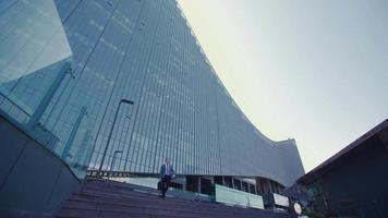 homme d'affaires moderne et immeuble d'affaires de luxe. homme d'affaires sort d'un immeuble de luxe et regarde sa montre. il descend les escaliers. homme d'affaires en costume avec sac. video