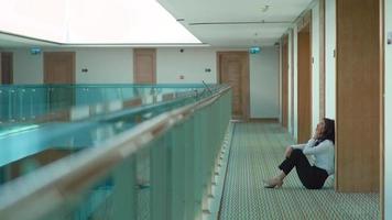 Sad businesswoman sitting on the floor in the hallway. Sad state of businesswoman sitting on floor in corridor. video