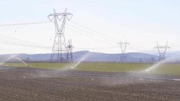 irrigação de terras agrícolas, sistema de irrigação por aspersão. aspersores irrigando terras agrícolas. o tempo está ensolarado e o solo é regado. video