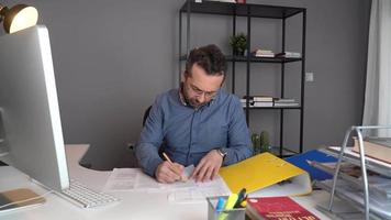 hombre trabajando duro en su oficina. el hombre que examina el papeleo frente a él está pensativo y estresado. video