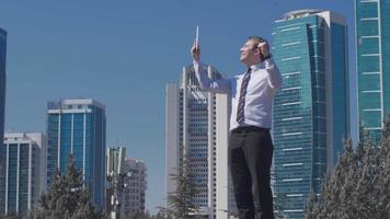 hombre de negocios regocijado, edificios comerciales de lujo. el hombre de negocios se regocija trabajando en una tableta frente a edificios comerciales de lujo. video