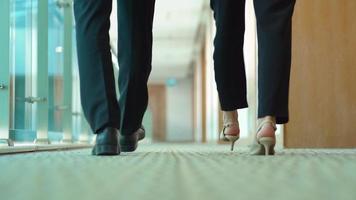 Businesswoman and businessman walking in the hallway. Businessman and businesswoman holding laptop are walking down the hall chatting. video