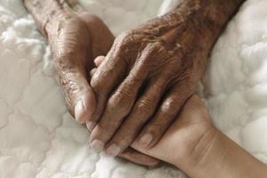 manos del anciano y la mano de un niño en la cama blanca en un hospital. foto