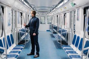 Shot of man who doesnt work at distance during quarantine, wears face mask to avoid coronavirus infection, poses in empty underground carriage with no people. Health awareness for pandemic protection photo