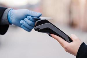 Cashless payment during quarantine. Hand in rubber gloves, credit card and payment terminal. Prevention of coronavirus spread. Good service during pandemic situation. Horizontal shot. Covid-19 photo