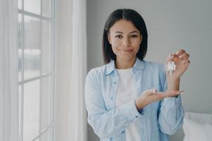 Satisfied hispanic girl holding house keychain in hand. Young woman is buying apartment and moving. photo