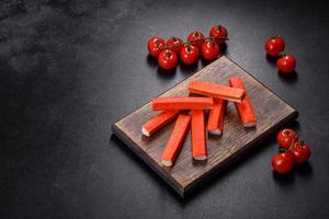 Crab sticks on a cutting Board with a knife. On black concrete background photo