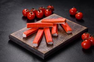 Crab sticks on a cutting Board with a knife. On black concrete background photo