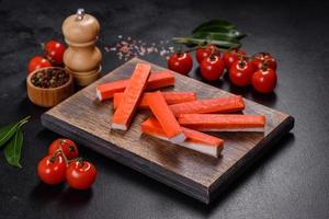 Crab sticks on a cutting Board with a knife. On black concrete background photo