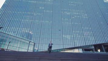 moderner geschäftsmann und luxusgeschäftsgebäude. Geschäftsmann kommt aus einem Luxusgebäude und schaut auf seine Uhr. Er geht die Treppe hinunter. Geschäftsmann im Anzug mit Tasche. video