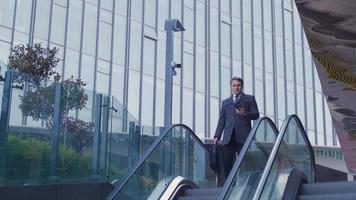 Businessman with bag going down escalator, angry phone call. Businessman with briefcase goes down escalators in front of a luxury business building. video