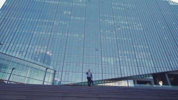 edificio di lusso e uomo d'affari che parla al telefono, allegro felice. uomo d'affari che esce da un edificio di affari di lusso parlando al telefono. è felice e allegro. video