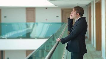 Businessman talking on the phone in the hallway. A man walking down the aisle at work is talking on the phone. Corporate and modern looking businessman. video