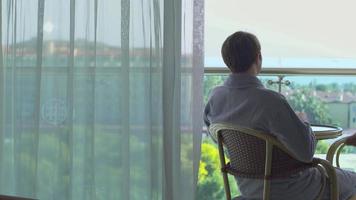 uomo che beve caffè sul balcone dell'hotel. uomo seduto sul balcone in vestaglia e bevendo il suo caffè. balcone dell'hotel. video