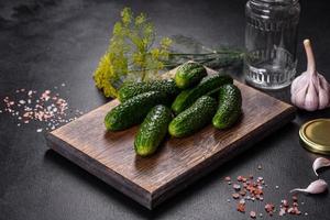 deliciosos pepinos frescos con ajo, sal, especias y hierbas en una tabla de cortar de madera foto