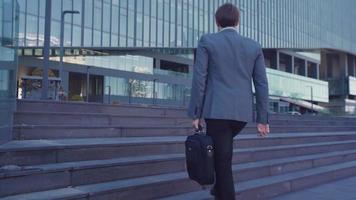 uomo d'affari con valigetta che cammina verso l'edificio. un uomo d'affari in giacca e cravatta che porta una valigetta si dirige verso l'edificio degli affari. video