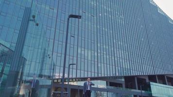 Happy businessman and exit from luxury building. Businessman comes out of a luxury building and looks at his watch. Businessman in suit with bag. video
