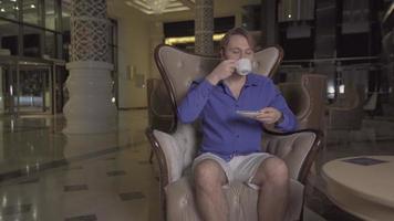 o homem tomando seu café no saguão do hotel. o homem esperando no saguão do hotel está bebendo seu café e descansando. video