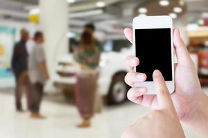 hands holding mobile phone with new cars in showroom photo