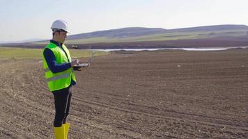 Engineer working in farmland. Engineer standing on earthen land working with laptop. He's doing analysis. He is taking notes on the laptop. Modern and technological agriculture. video