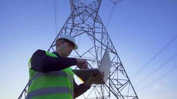 ingenieur, der vor strommasten arbeitet. Ingenieur, der vor Strommasten am Laptop arbeitet. Durchführung von Felduntersuchungen. Elektroingenieur. video