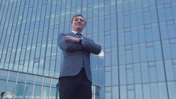 Luxury buildings and businessman. Businessman looking at camera in front of luxury buildings folds his arms and smiles.  Modern businessman in suit.