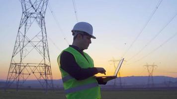 engenheiro examinando postes elétricos. engenheiro trabalhando no laptop ao pôr do sol e olhando para postes elétricos. pesquisa de campo e reviso video