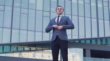 Confident young businessman in suit. Young businessman standing in front of luxury building buttoning his jacket. video